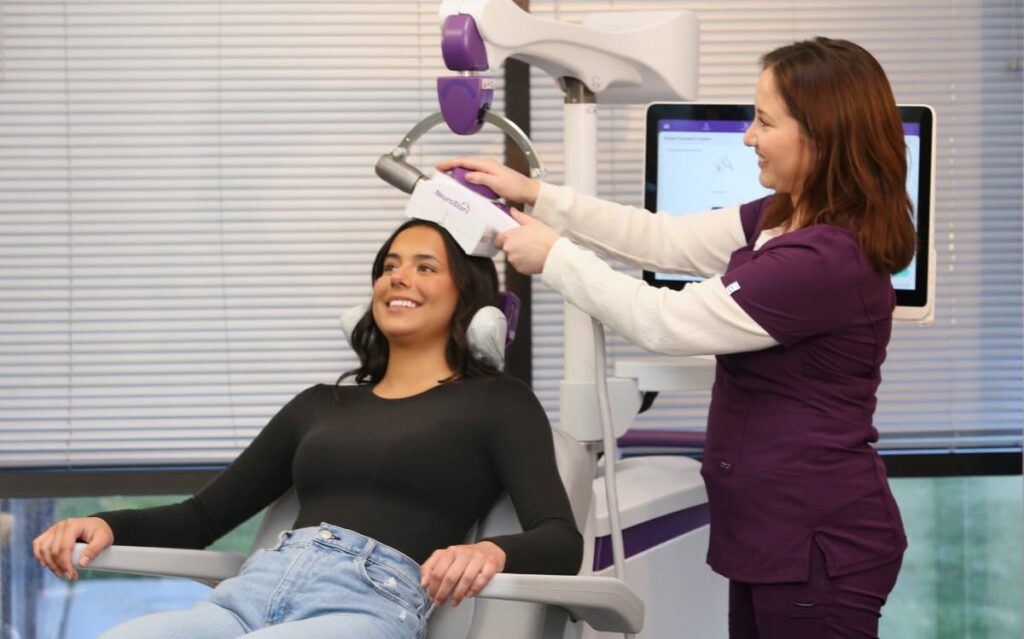 A patient smiling during a TMS session ,  What is the Success Rate of TMS? ,  as a technician positions the NeuroStar device.