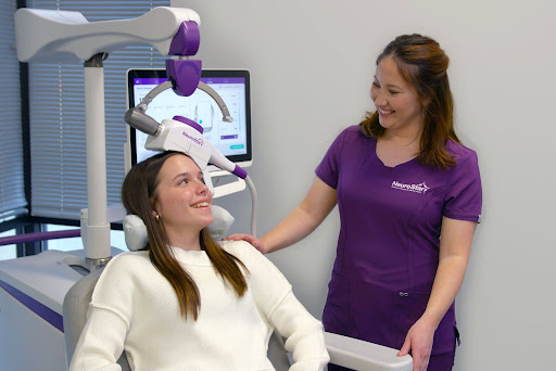 A smiling patient asks, does TMS really help with depression? as a NeuroStar technician administers TMS therapy. 