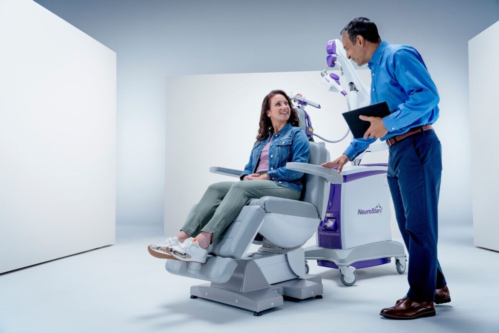 Can OCD be treated with TMS? Patient smiling during a NeuroStar TMS session with a doctor nearby. 