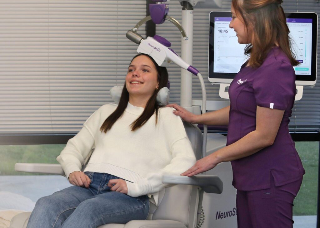 Smiling teen receiving non-invasive NeuroStar TMS therapy from a trained clinician.