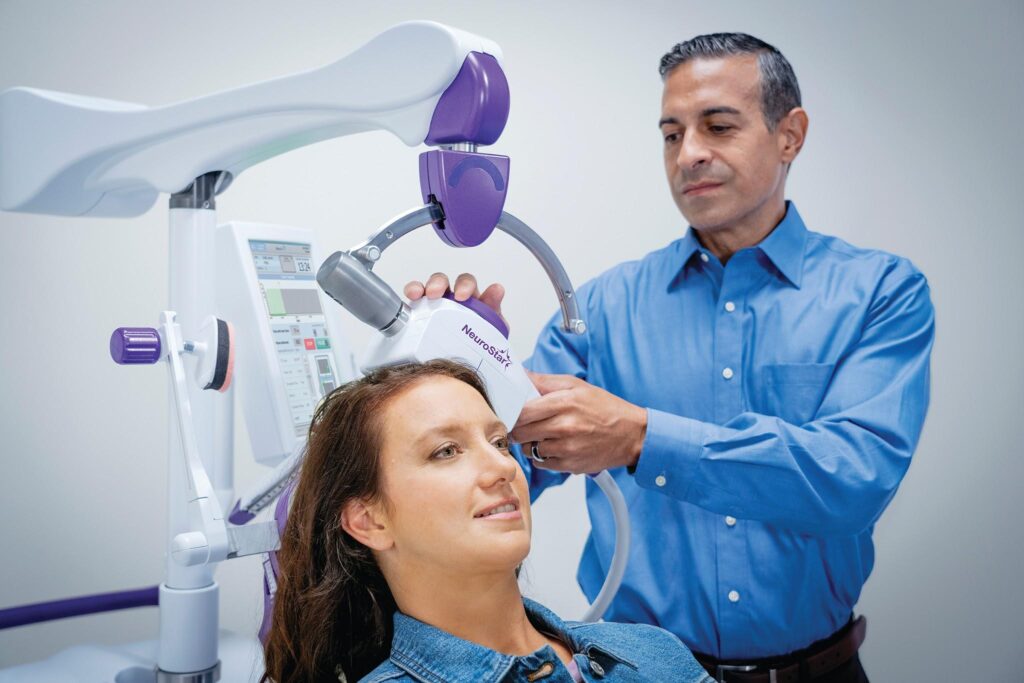Doctor positioning NeuroStar TMS coil above a seated female patient's head during treatment.